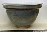 Side view of large handmade pottery bowl showing curved shape, flared rim, and muted blue-gray glaze with speckles.