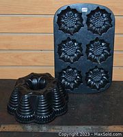 Photo showing a sunflower-shaped muffin pan with six flower-design cups and a beehive pattern bundt pan arranged side by side on a wooden surface.