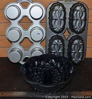 Three Nordic Ware baking pans together: a six-cup muffin pan, a four-cup hot dog shaped mold pan, and a bundt cake pan with floral design
