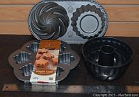 Five Nordic Ware baking pans shown on table including black Bundt pan, muffin pan, and 3 decorative pans with star and cupcake shapes