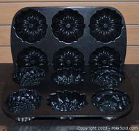 Top and angled front view of one black metal mini Bundt cake pan with 6 floral-shaped cavities.
