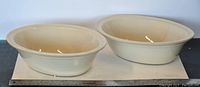 Two oval off-white ceramic pot pie dishes side by side with a ruler beneath showing about 11 inches length each