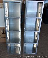 Full view of two tin shelving units standing side-by-side on a carpeted floor showing their height and three shelves each.