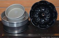 Photo showing the stacked round cake pans next to the black Bundt pan on a wooden background with a ruler in front for scale.