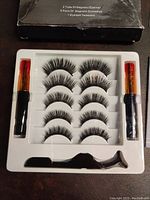 Top view of the kit showing two magnetic eyeliner tubes, five pairs of magnetic eyelashes arranged in a plastic tray, and a black eyelash tweezer.