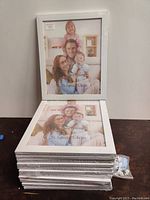 Stack of 12 white picture frames, factory sealed in shrink wrap, showing the front with a sample photo insert, measuring 8x10 inches.