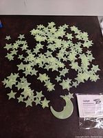 Many pale green glow in the dark star-shaped stickers and one crescent moon-shaped sticker laid out on a dark flat surface with an instruction sheet visible.