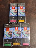 Five sealed boxes of Arteza acrylic markers in different colors arranged on a surface.