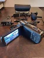 Open LCD touchscreen display shows camera interface with video preview. Various cables and accessories are visible on table.