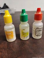 Three small bottles of gold testing solutions with yellow, green, and red caps labeled 10K, 14K, and 18K respectively.