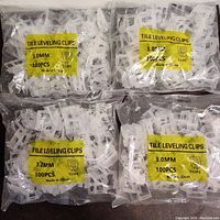 Four sealed plastic bags each containing 100 white tile leveling clips with yellow labels stating 'TILE LEVELING CLIPS 3.0MM 100PCS Made in China'.