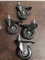 Four brand new black urethane swiveling caster wheels with brake levers and mounting bolts.