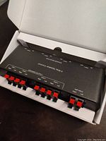 Speaker controller device opened inside white box. Top panel visible with speaker output terminals and controls.