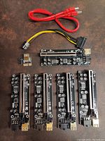 Full view of five PCI-E riser cards, along with a red USB 3.0 cable and a yellow-black 6-pin power cable against a brown surface.