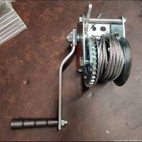Full view of the hand crank winch showing the handle, ratchet gear, and cable drum with steel cable.