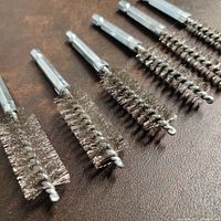 Six steel wire twisted bore cleaning brushes with 1/4 inch hex shank arranged in a row, varying diameters visible, placed on brown surface.
