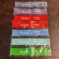 Seven sealed elastic workout resistance bands laid flat on a black surface showing colors and labels: two blue XX-Heavy, one purple XX-Heavy, two red X-Heavy, one turquoise Medium, and one green Light.