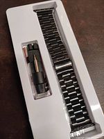 Satin black stainless steel link bracelet with pin pusher tool secured in white plastic packaging.