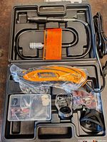 Rotary tool with flexible shaft, safety guard, sanding drums, and other accessories arranged in a black molded plastic carrying case.