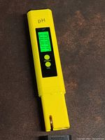 Yellow digital water pH tester device turned on showing green LCD screen with pH reading and buttons.