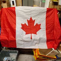 Full front view of the large Canada flag hanging unfolded showing the red maple leaf centered on white field with red vertical stripes on each side. The fabric appears synthetic with visible light creasing.
