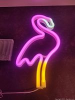Pink flamingo neon sign illuminated on a wall showing pink, white, and yellow colors.