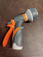 Side view of the sprayer showing ergonomic grey handle with orange trigger and grey nozzle head with orange accent.
