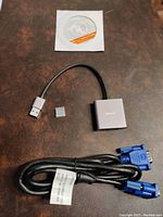 Full lot showing USB 3.0 to VGA adapter, VGA cable, small USB connector cap, and driver disc on brown surface