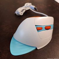 Side angle view of the vertical ergonomic mouse showing the white body, light blue thumb rest, orange scroll wheel and buttons, and USB cord.