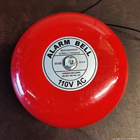 Front view of a red metal alarm bell, showing the circular label indicating specs: weatherproof, 6 inch size, 95dB, 25mA, 110V AC.