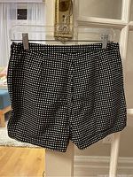 Front view of the black shorts with white polka dots on hanger against a door