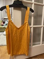 Marigold sleeveless top hanging on a hanger in front of a door; V-neck visible