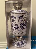 Front view of the Greek-style drink dispenser inside unopened box showing purple floral design and silver spigot.