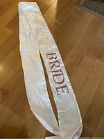 White satin sash laid out on wooden floor, showing full length with 'BRIDE' text