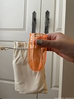 Orange glass held over white drawstring pouch, showing the shape and color of the glass.