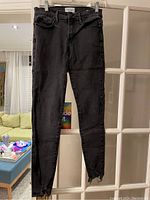 Front view of charcoal Frame jeans size 27 hanging on hanger, showing zipper details on ankles.