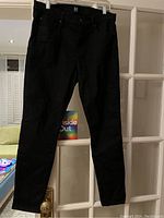 Front view of black Gap jeans hanging on hanger against glass door.