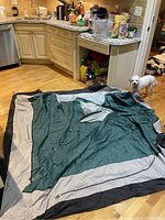 Green and beige tent fabric spread on wood floor with a small white dog nearby, showing size and condition of tent material.