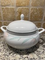 Front view of the ivory-colored porcelain soup tureen with floral design, showing two handles and lid with knob.