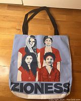 Blue tote bag with black handles showing 4 diverse individuals wearing red tops and Star of David necklaces, with text 'ZIONESS'