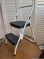 Side view of the two-step folding stool showing the aluminum frame, black rubber steps, and foldable handle.