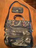 Top view of black Fossil leather handbag with multiple zippered compartments and brown leather buckle accents, along with matching black wallet