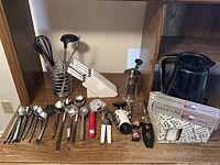 Photo showing the entire assortment of kitchen cutlery, utensils, wine openers, kettle, pepper grinder, and salad tongs on a wooden shelf.