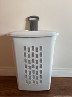 White plastic laundry hamper with ventilation holes, lid, and gray extendable handle, angled front side view