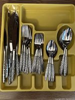 Full flatware set organized in yellow tray including knives, forks of two sizes, spoons of two sizes all with patterned handles.
