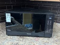 Closed front view of black Panasonic microwave on countertop with control panel on the right.