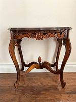 Side view of the antique walnut end table showing carved floral apron and curved legs.