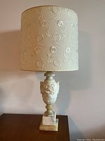 Front view of vintage alabaster lamp with floral carved base and off-white embossed fabric lampshade