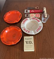 Photo showing the two orange Frontenac ashtrays, white Labatts ashtray, three bottle openers, Seagram's V.O. playing cards, and part of the Secretariat shot glass