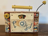 Front and side view of the vintage Fisher Price wind-up TV radio music box showing colorful indigenous-themed artwork and the winding crank.